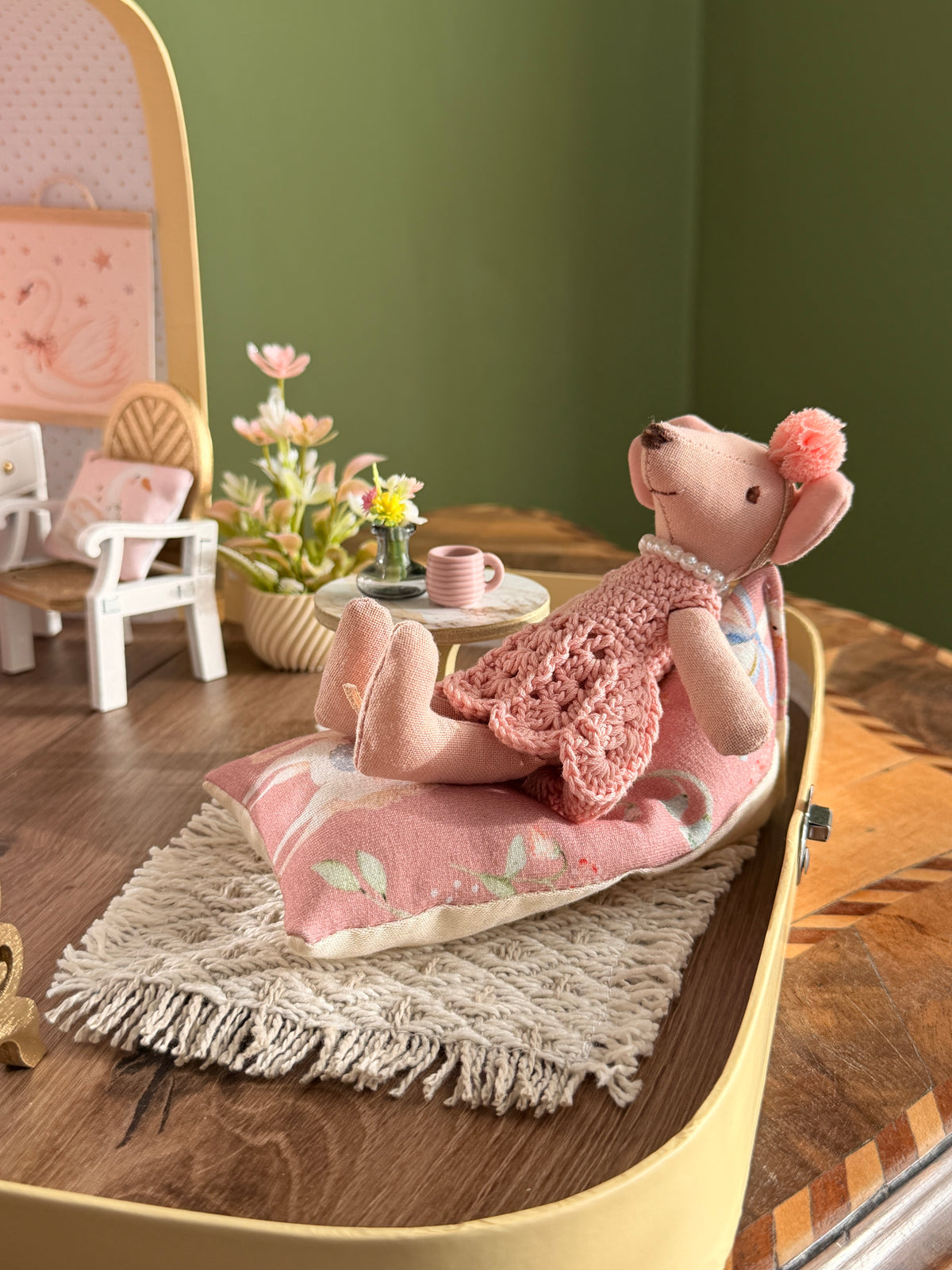 Ballerina mouse resting on a floor cushion on a fringed rug after the show, with a tiny pink cup and flowers