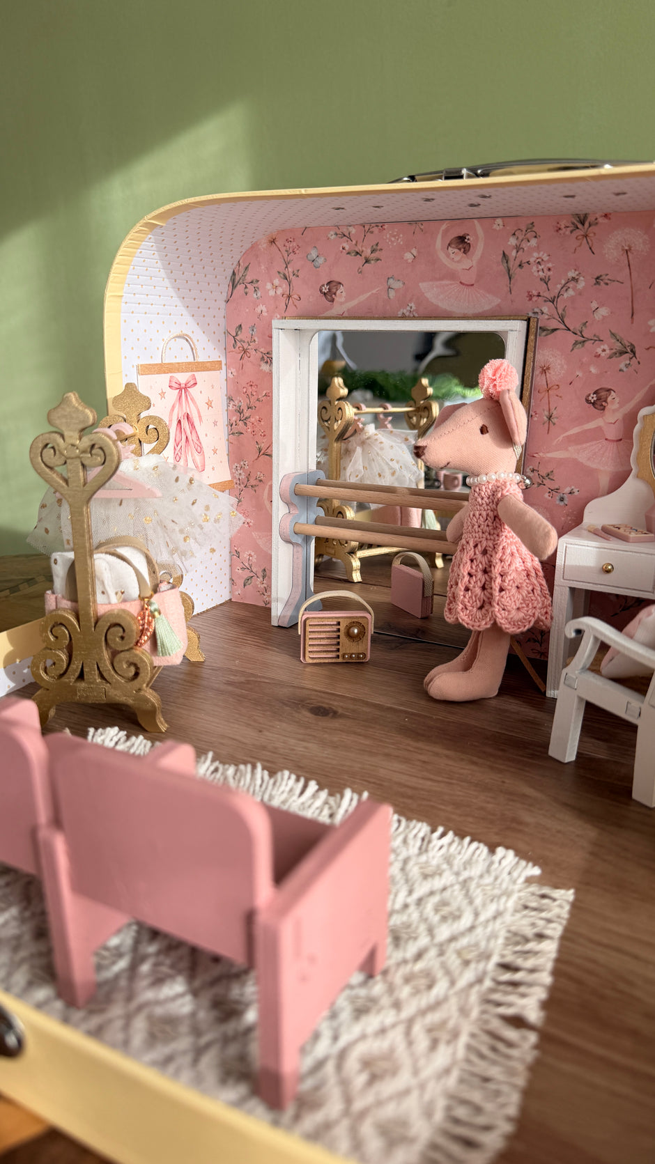 Inside the ballerina suitcase dollhouse: ballet barre with mirror, ballerina mouse, tutu on a gold stand and pink theatre seats