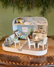 The Calm Grove – Koffer-Puppenhaus im mittleren Format mit grauem Sofa, rundem Esstisch, weißer Küche und Hochebene mit Teddybär